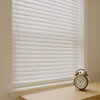 A bright living room with clean, well-maintained white horizontal blinds and an antique brass clock on the windowsill, symbolizing durability and long-lasting quality